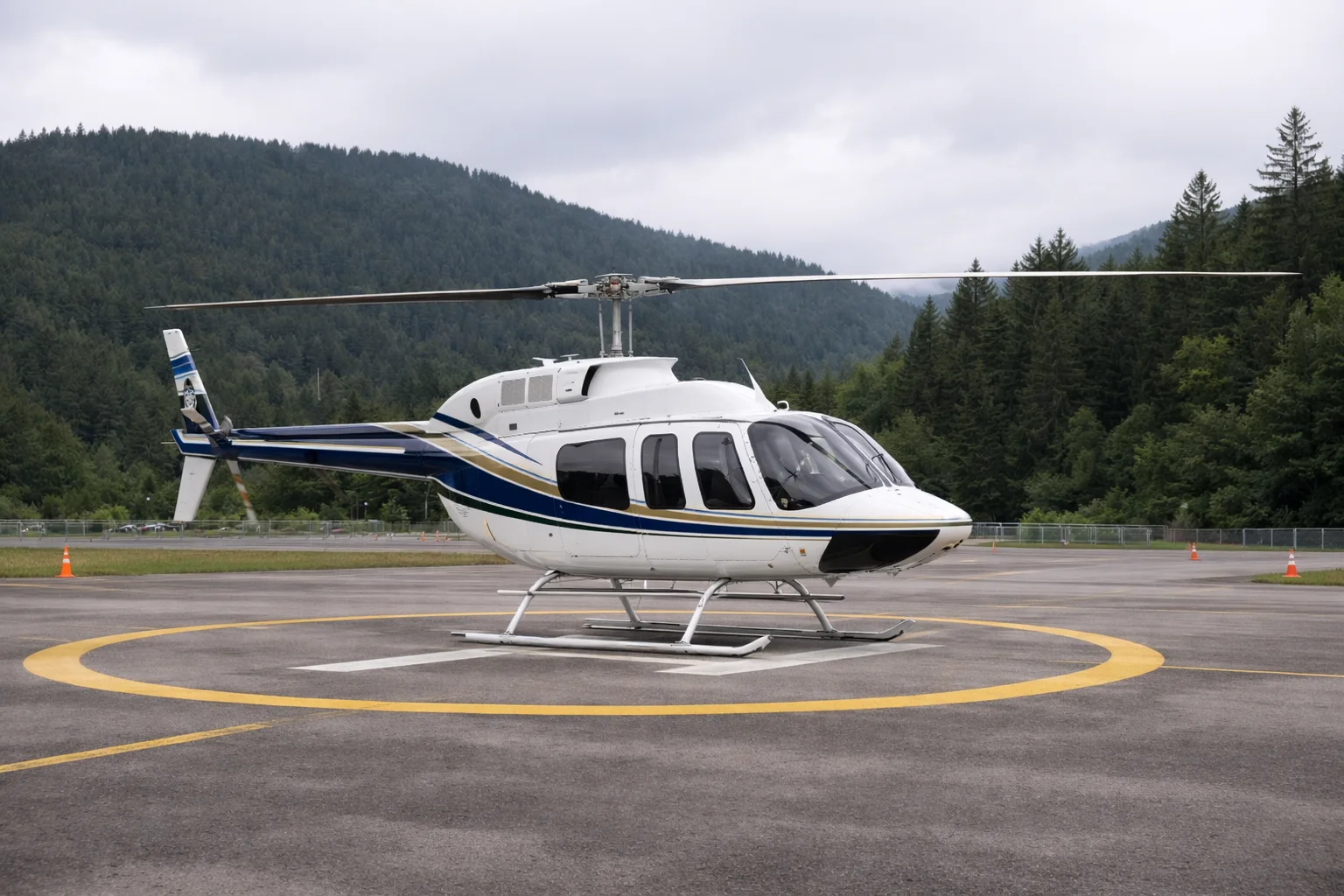 Bell 206L LongRanger style helicopter on a heliport pad near forested hills in overcast daylight